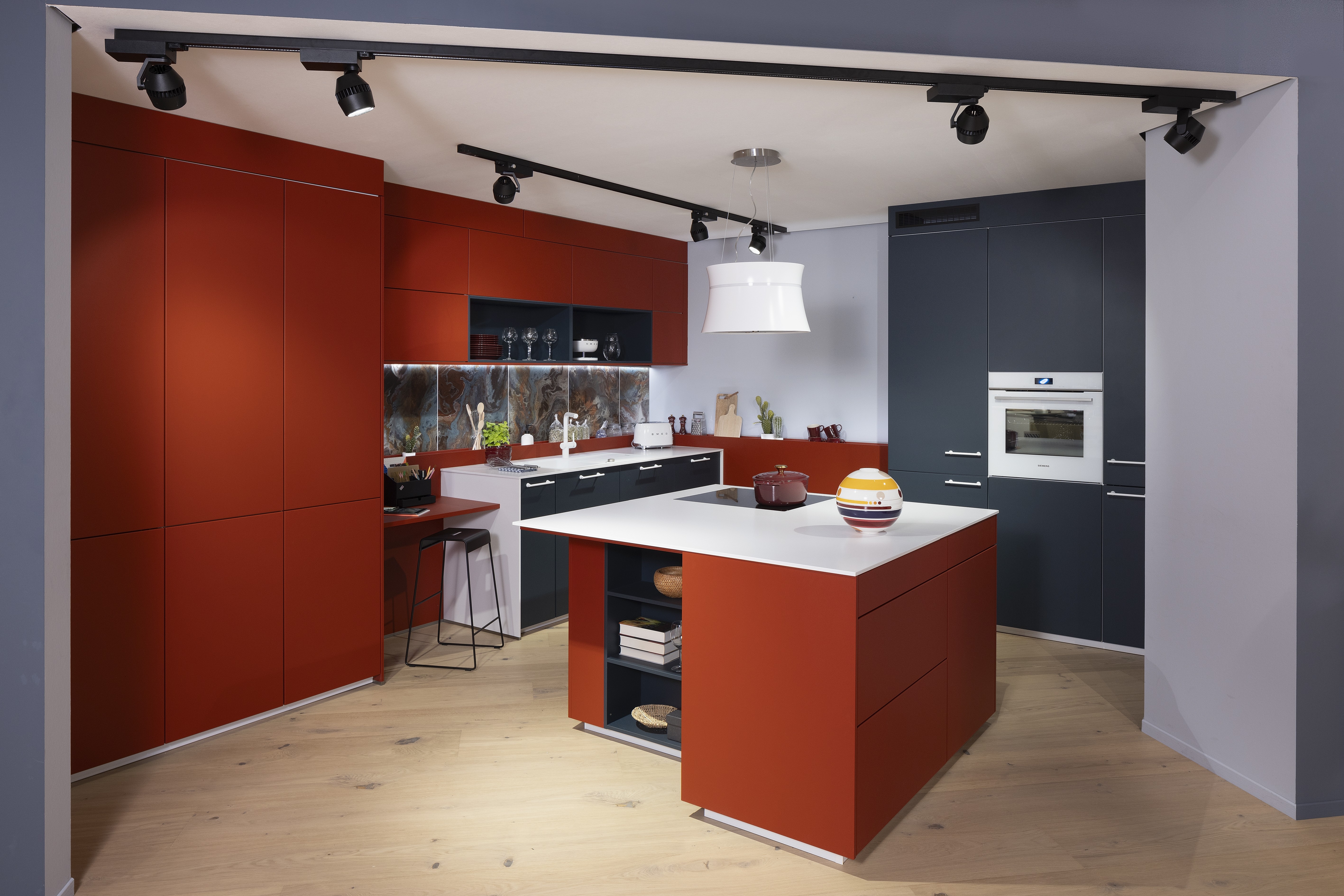 APL: Systeme Blanco Zeus matt Front: Herbstrot samtmatt AFP Front: Tiefblau samtmatt AFP Korpus: Kristallweiß/Naturweiß Griff: Metall Weiß lackiert Geräte: Siemens, Abzugshaube Airforce Armatur: Franke Spüle: Franke   Features: Farbe in der Küche, quadratische Kücheninsel mit Kochfeld und Dunstabzug, Kontrastelemente in Weiß (Griffe, APL, Spüle, Wasserhahn und Backofen), weißer BACKOFEN, kleine Designküche, junge Küche, Nischenrückwand als Motivfliese (Schüller), Arbeitsplatz, „versteckte“ Kaffeeküche 