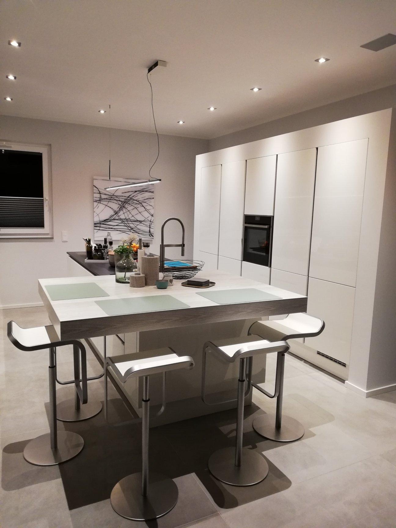 Kücheninsel mit überstehender Platte und Barhockern, dahinter eine Hochschrankzeile