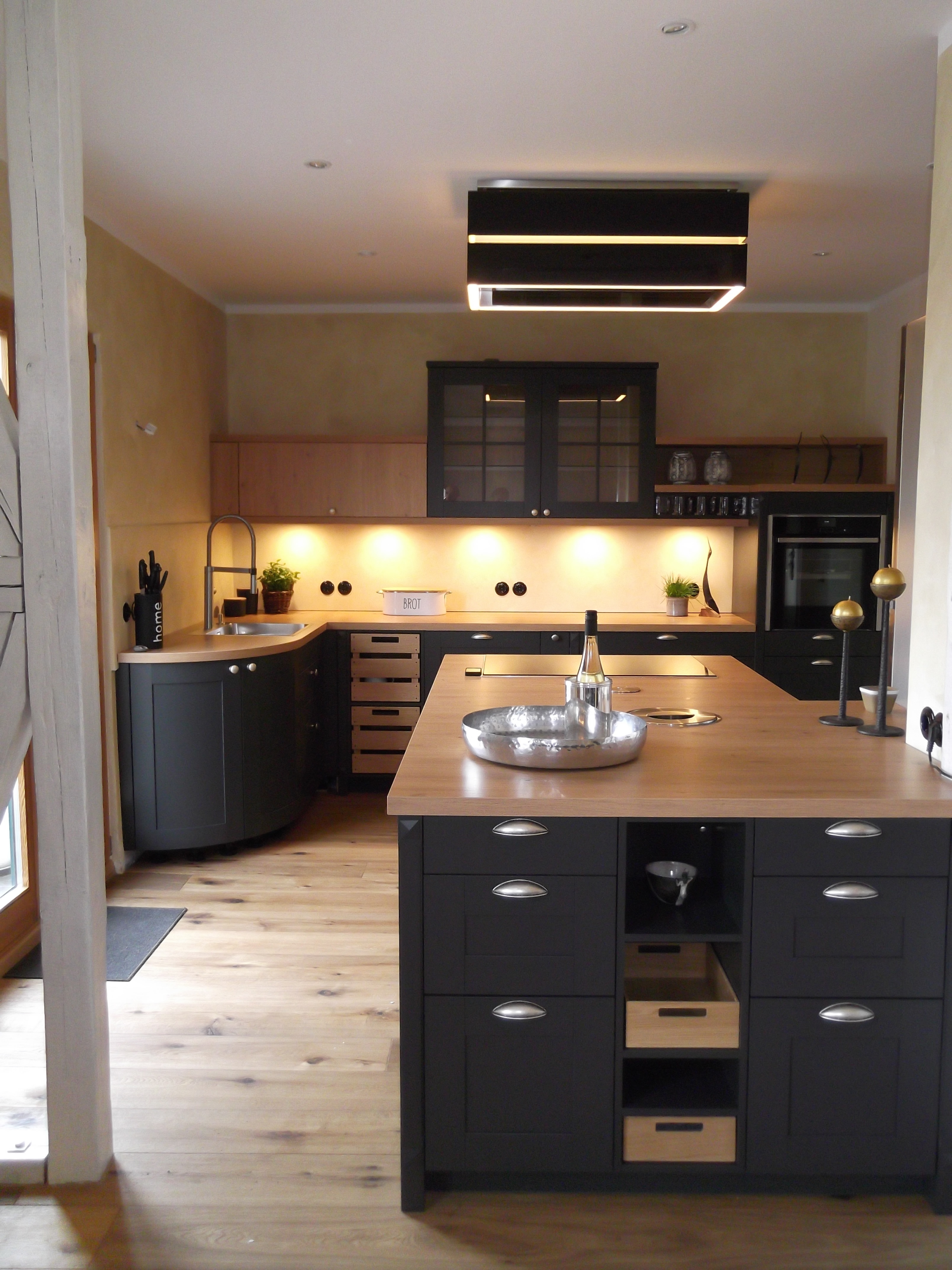 Schwarze Landhausküche mit Holzelementen und Holzarbeitsplatte mit abgerundeten Schränken und einer Kücheninsel