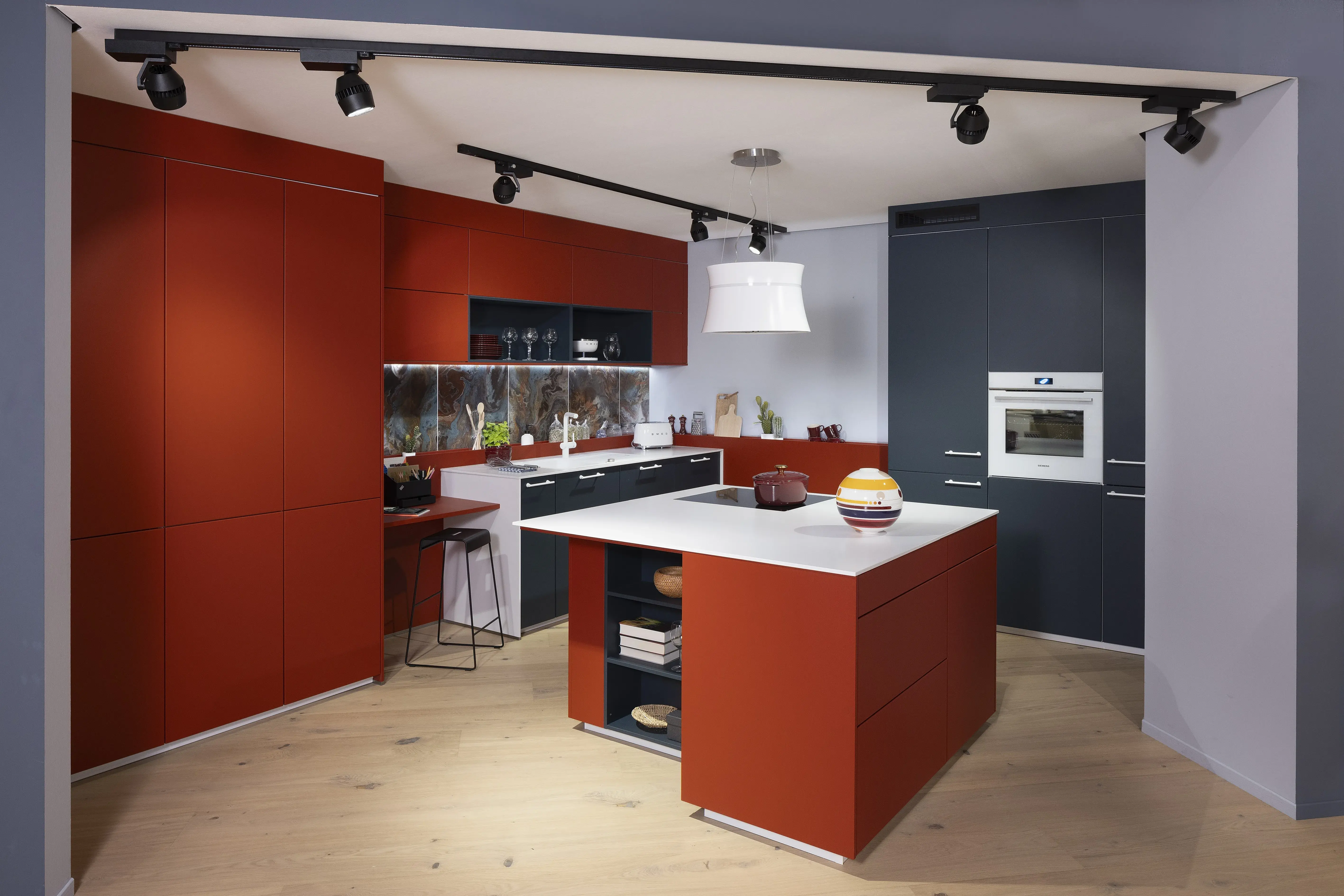 APL: Systeme Blanco Zeus matt Front: Herbstrot samtmatt AFP Front: Tiefblau samtmatt AFP Korpus: Kristallweiß/Naturweiß Griff: Metall Weiß lackiert Geräte: Siemens, Abzugshaube Airforce Armatur: Franke Spüle: Franke   Features: Farbe in der Küche, quadratische Kücheninsel mit Kochfeld und Dunstabzug, Kontrastelemente in Weiß (Griffe, APL, Spüle, Wasserhahn und Backofen), weißer BACKOFEN, kleine Designküche, junge Küche, Nischenrückwand als Motivfliese (Schüller), Arbeitsplatz, „versteckte“ Kaffeeküche 