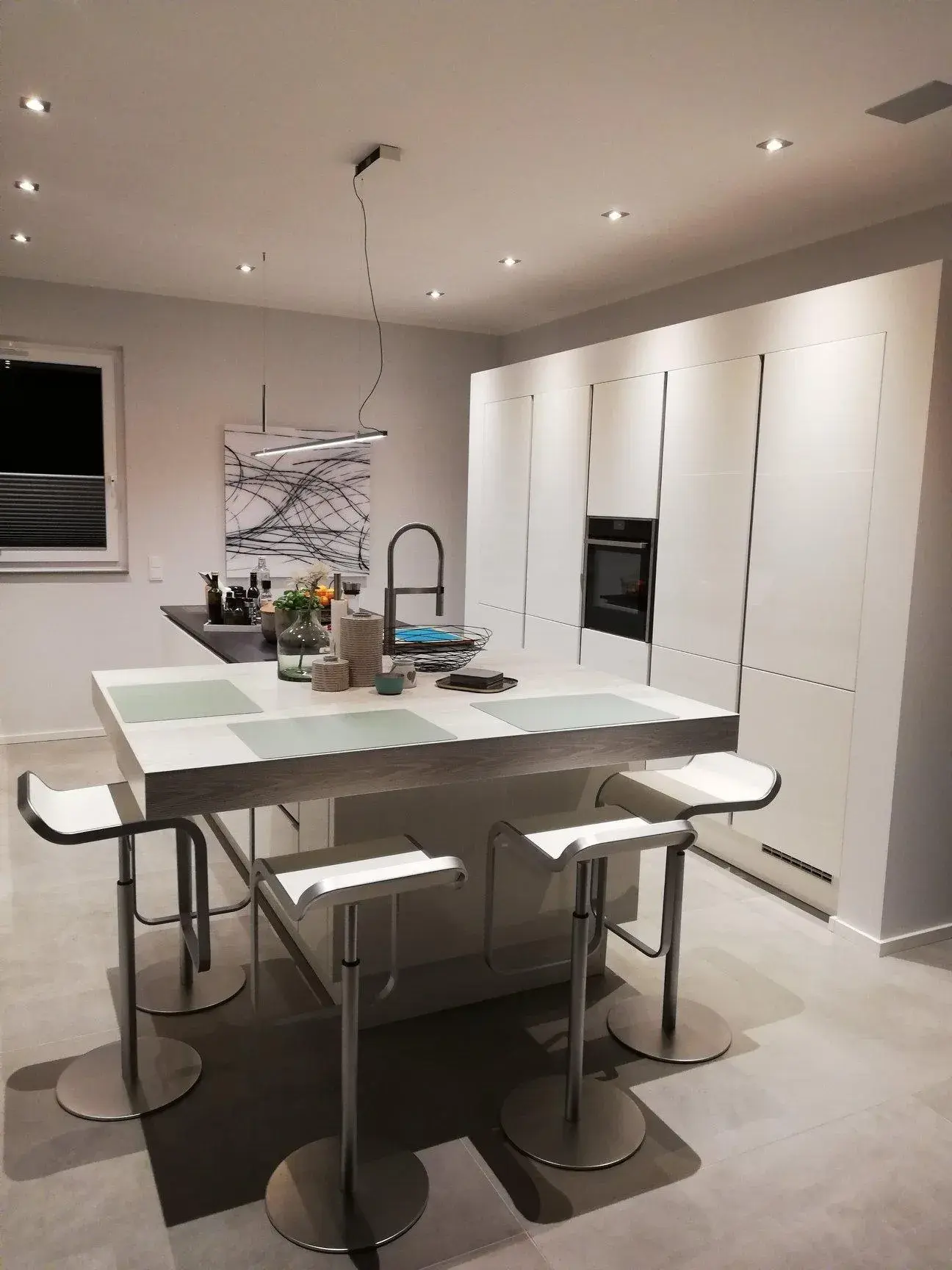 Kücheninsel mit überstehender Platte und Barhockern, dahinter eine Hochschrankzeile